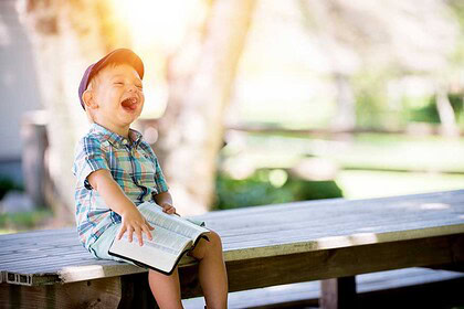 Little boy sitting on a bench, reading and lauging