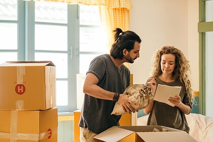 moving boxes with a man unpacking and a woman checking list.